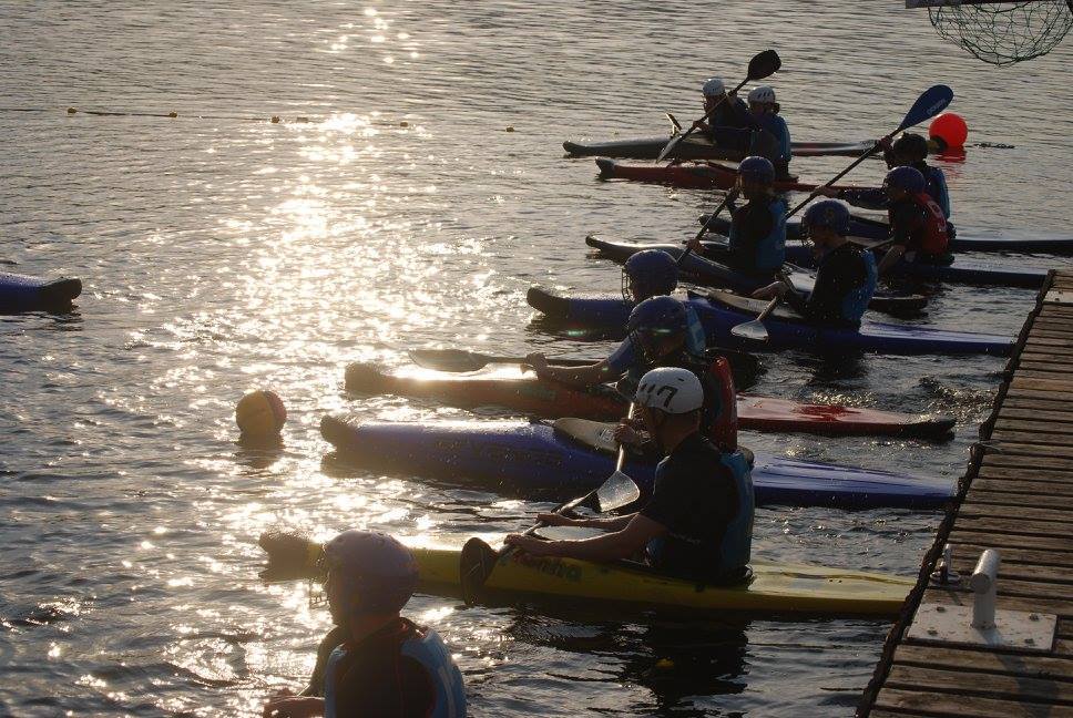 Paddlers lined up beside a pontoon with sunlight reflecting on the lake.